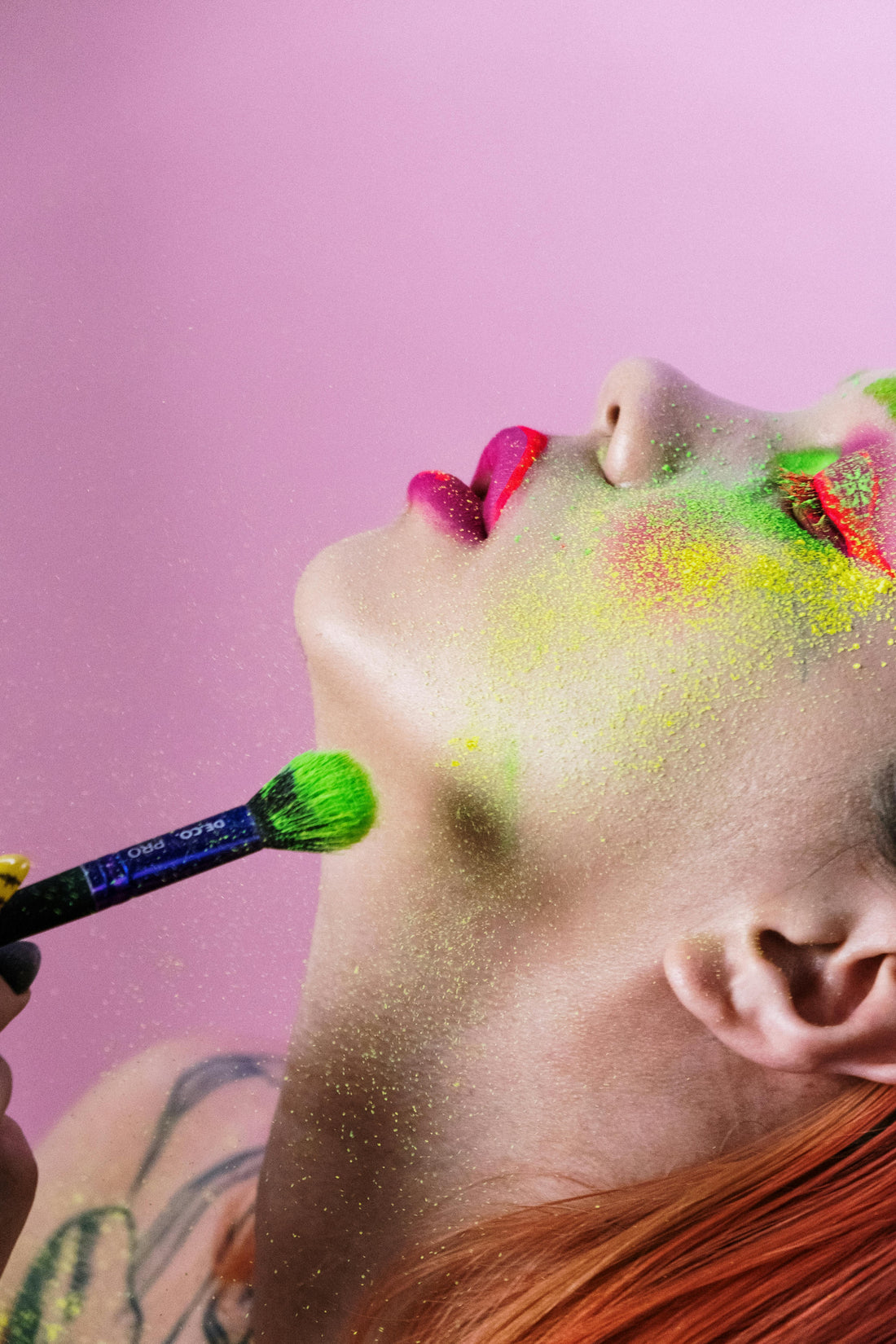 Person applying colorful makeup with a brush against a pink background