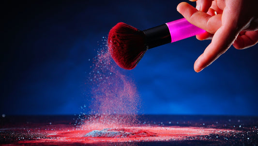 Hand holding a makeup brush with red powder against a dark background