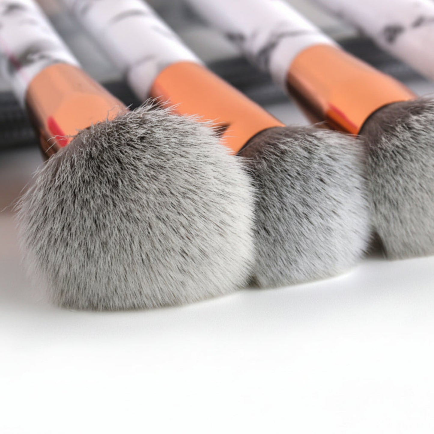 Close-up of makeup brushes with gray bristles and orange handles on a white background