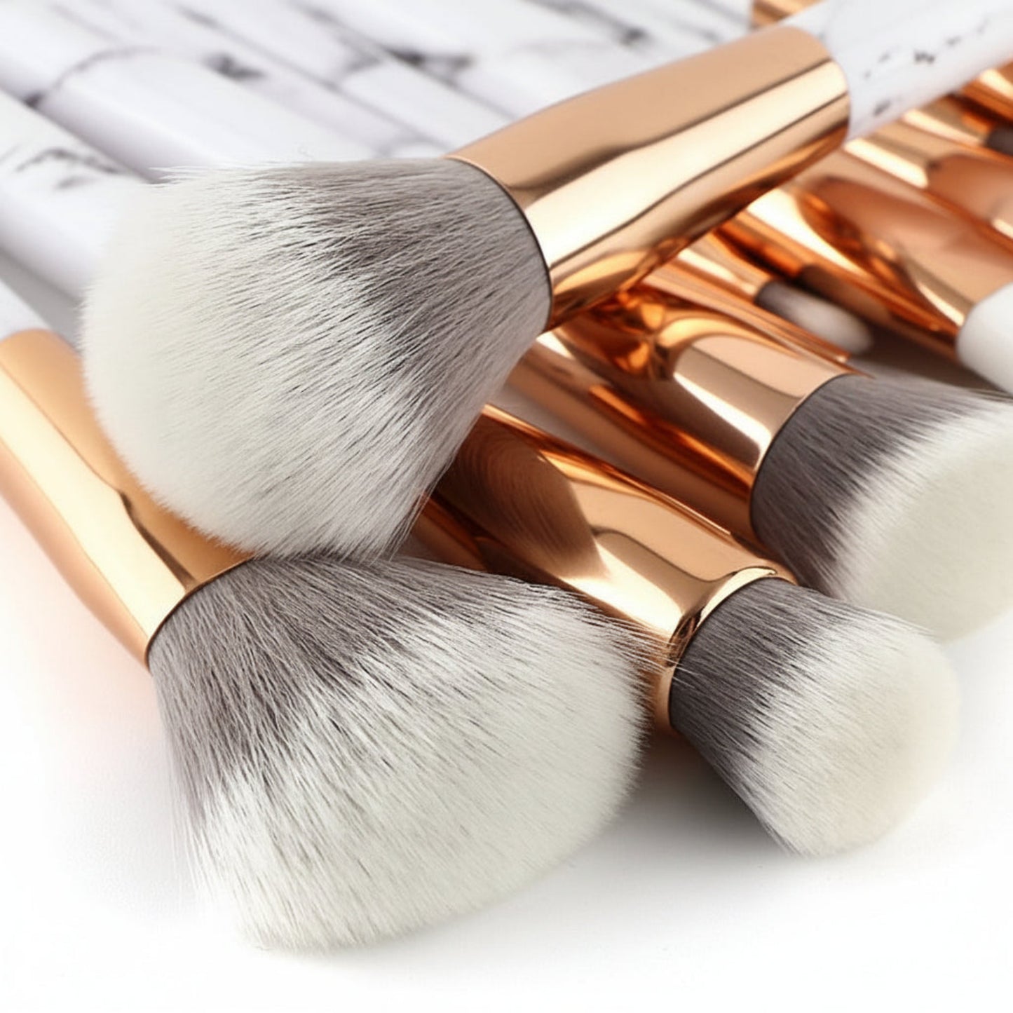 Set of rose gold makeup brushes with white bristles on a light background
